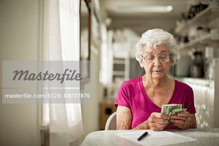 Anxious elderly woman sorts through her money to see if she has enough to pay the bill in front of her.
