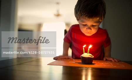 Young boy blowing out three candles on his birthday cupcake.