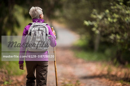 Mature woman goes for a hike along a leafy forest trail.