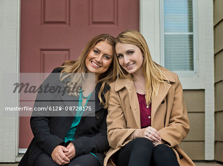 Portrait of two smiling young women sitting on the porch of their home.