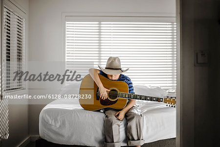 Young boy sitting on his bed with his acoustic guitar.