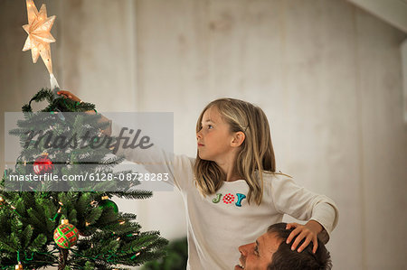 Young girl placing the star on the top of the Christmas tree with her father. Young girl placing the star on the top of the Christmas tree with her father.