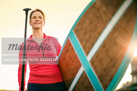 Mid adult woman walking paddleboard to water.