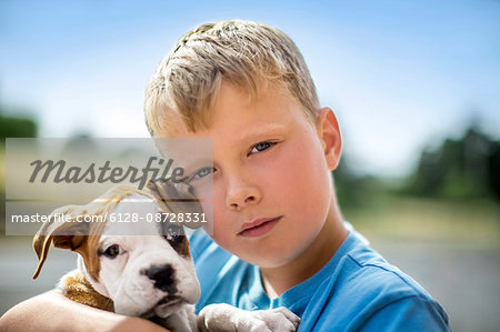 Portrait of a young boy holding his bulldog puppy.