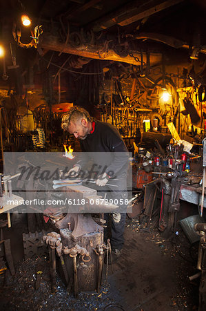 Blacksmith standing at an anvil in his workshop.