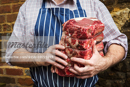 Butcher in blue striped apron holding a large piece of beef.