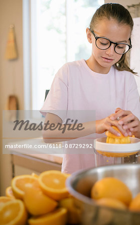 Family preparing breakfast in a kitchen, girl squeezing oranges.