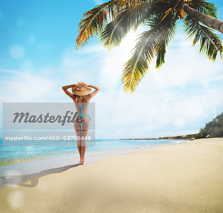 Girl with straw hat walking on the beach with palm trees