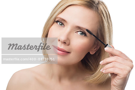 Beautiful middle aged woman with smooth skin and short blond hair applying fix gel to eyebrows. Beauty shot. Isolated over white background. Copy space.