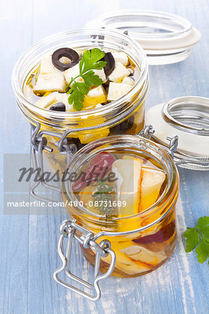 Marinated cheese in glass jar on blue wooden background. Culinary cheese eating.