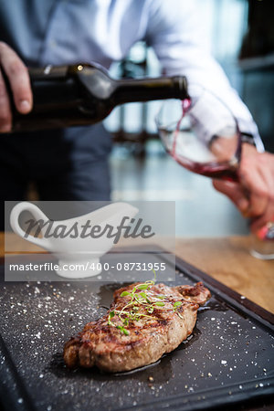 New York steak with waiter pouring red wine on background