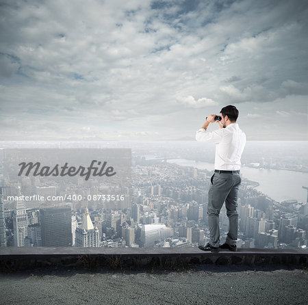 Businessman looks at the city from the roof with binoculars
