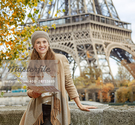 Autumn getaways in Paris. smiling young tourist woman on embankment in Paris, France  holding map and looking into the distance