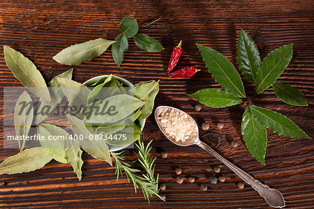 Traditional spice and condiment wooden background. Bay leaves, rosemary, chillies and black pepper on brown wooden table, top view.