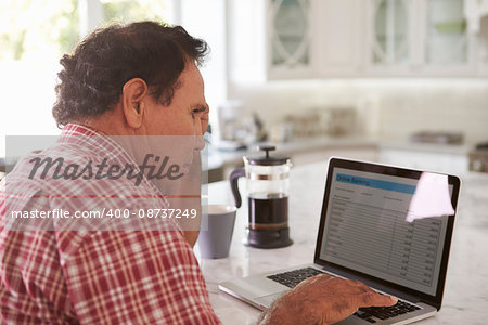 Confused Senior Hispanic Man Sitting At Home Using Laptop