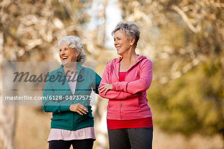 Two laughing senior women standing together in a park.
