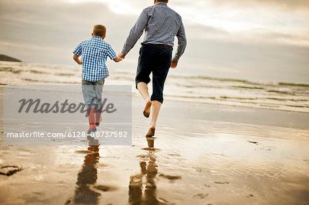 Mid-adult man running hand in hand with his son on the back..