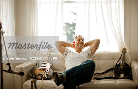 Mid-adult man sitting on a couch with two guitars in his living room.