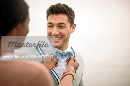 Young woman fixing a smiling young man's tie.