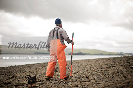 Senior man walking along a rocky shoreline.