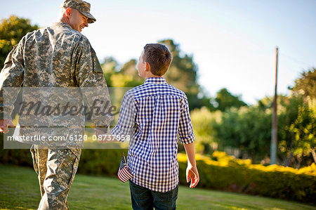 Male soldier holding hands with his son in their back yard.