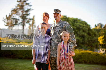 Portrait of a smiling male soldier standing with his family in the back yard of their home.