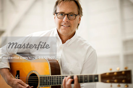 Portrait of a grinning mid adult man playing an acoustic guitar.