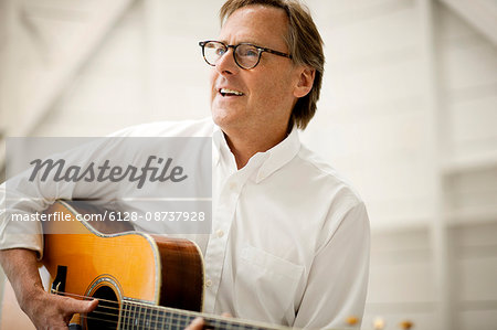 Smiling mid adult man playing an acoustic guitar inside a garage.