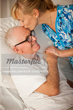 Smiling senior man being comforted by a female nurse while lying in bed.