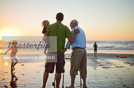 Senior man with a walking aid on the beach with his son and grandchild.