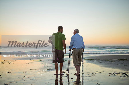 Senior man with a walking aid on the beach with his son and grandchild.