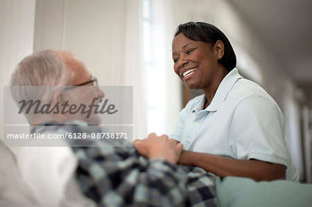 Happy female nurse comforting an elderly patient at his bedside.