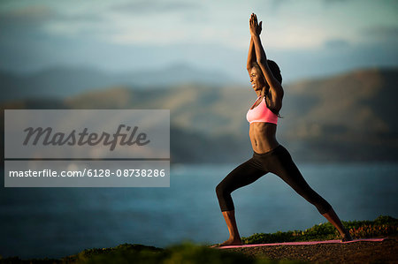 Young woman standing in a yoga pose near a coastline.