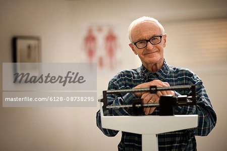 Portrait of a senior man weighing himself on scales in a doctor's office.