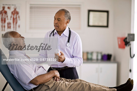 Male doctor having a conversation with a patient while holding a bottle of medication inside his office.