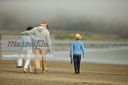 Senior couple walking on a beach with their young grandson.