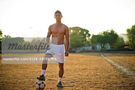 Portrait of a young soccer player standing with his foot on a ball while on a playing field.