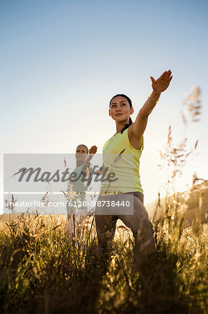 Two women practicing yoga in a rural field.