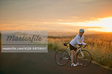 Smiling mature woman standing with her bike on a rural road.