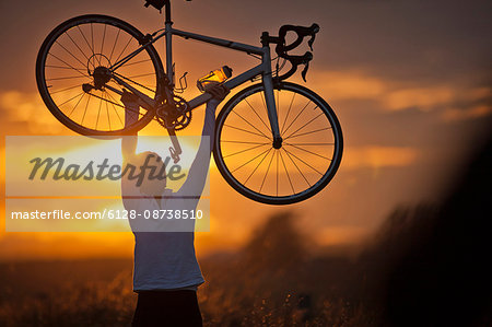 Smiling mature woman holding a bike above her head.