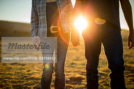 Farmer and his wife holding hands and walking through the fields of their ranch at sunset.