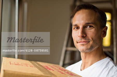 Portrait of a handsome young man smiling as he carries a cardboard box into his new home on moving day.