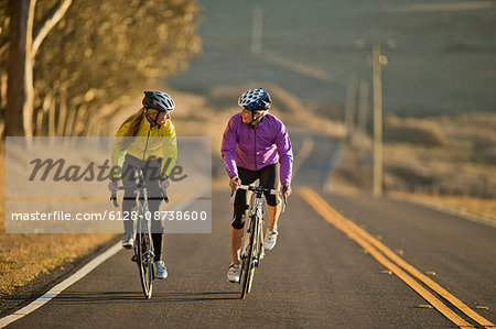 Two smiling young women cycling together down a country road.
