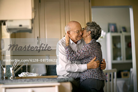 Affectionate elderly couple sneak a romantic kiss in the kitchen.