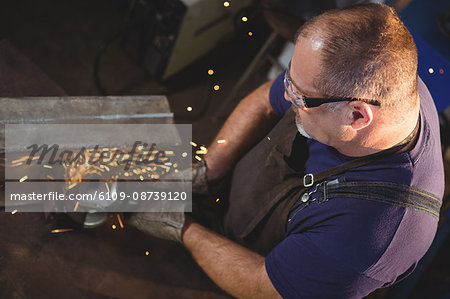 Welder cutting metal with electric tool in workshop