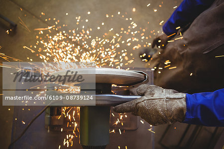 Mid-section of welder cutting metal with electric tool in workshop
