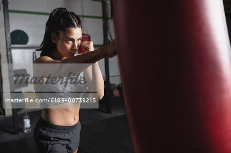 Female boxer practicing boxing with punching bag in fitness studio