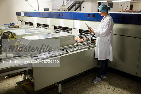 Female staff using digital tablet next to production line in egg factory