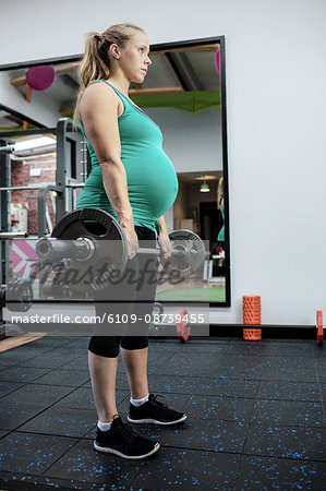 Pregnant woman working out with barbell at gym