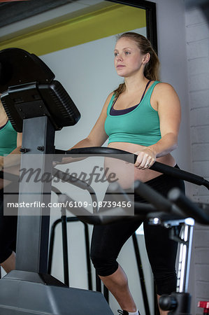 Pregnant woman exercising on elliptical machine at gym